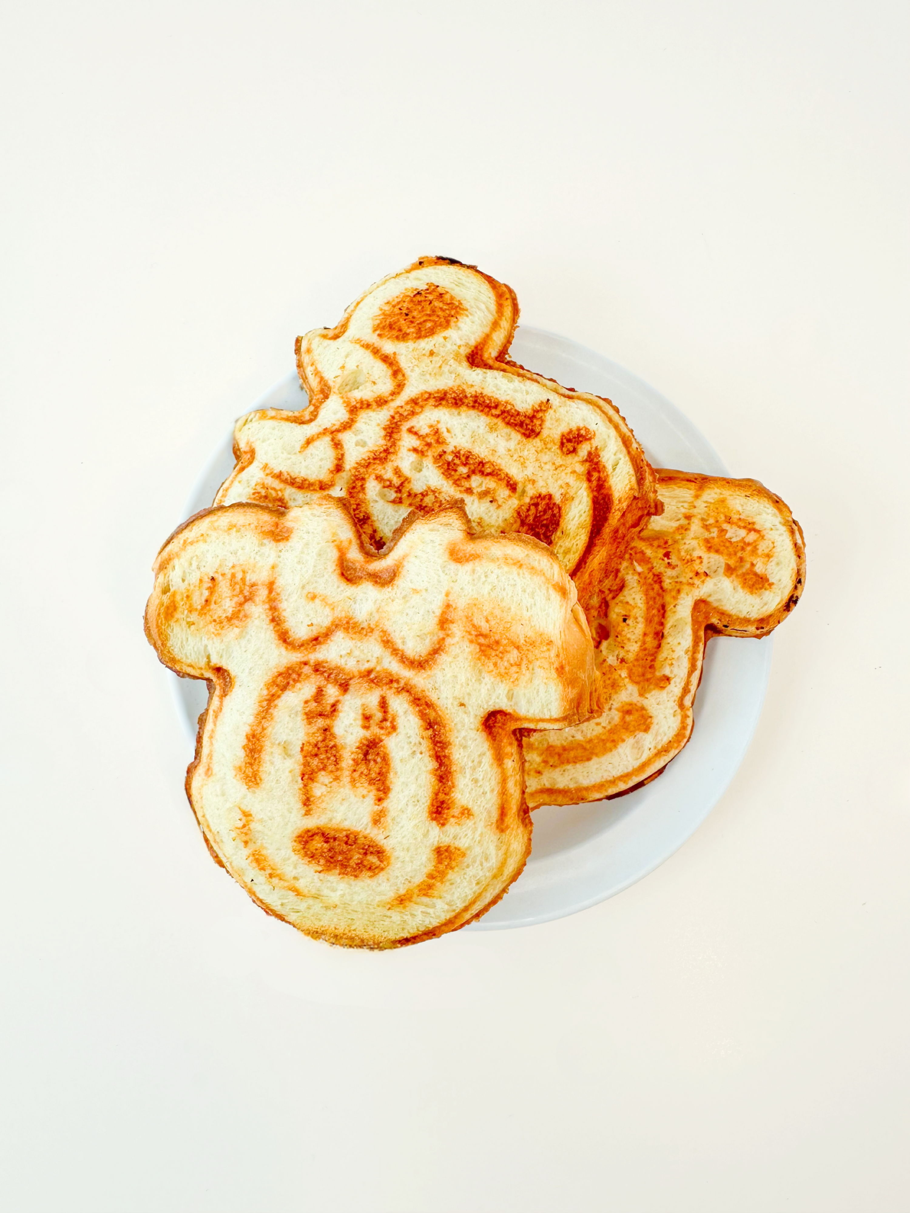 three minnie mouse and mickey mouse shaped grilled cheese stacked on each other on a white plate against a white background