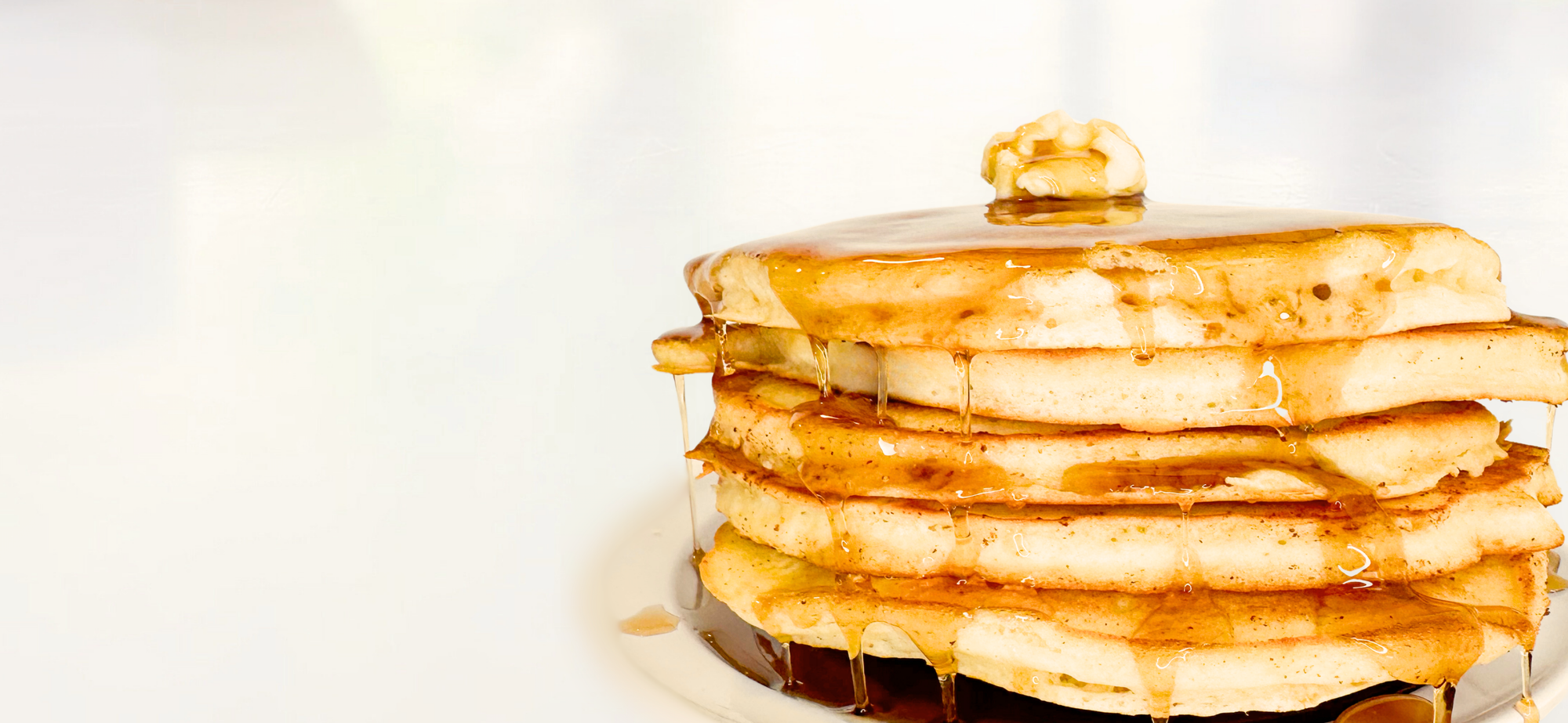five buttermilk pancakes stacked on top of each other with syrup and butter on a white background